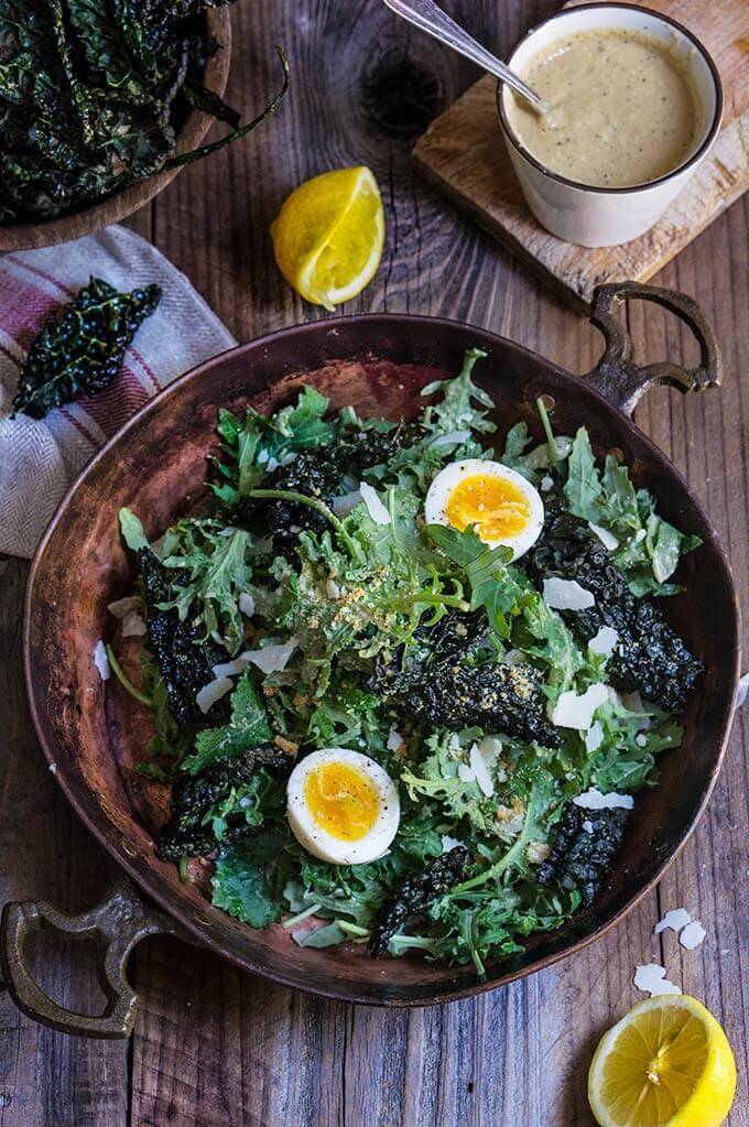 Kale salad with low fat Caesar dressing - baby kale and roasted kale chips, garlicky bread crumbs, and soft boiled eggs, drizzled with a healthy Caesar dressing which is packed with protein, low in fat, yet creamy and robust in flavor. | www.viktoriastable.com